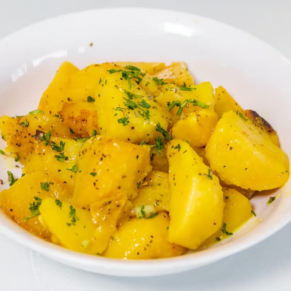 A white bowl filled with golden Greek lemon potatoes, garnished with parsley and black pepper.