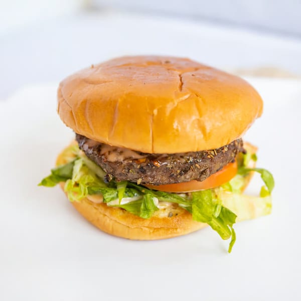 A Fat Greek burger with a seasoned patty, lettuce, tomato, and sauce on a brioche bun.