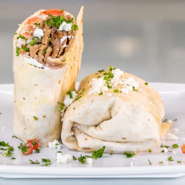 Two Greek gyros, one upright and one lying down, filled with meat, feta, tomatoes, and parsley.