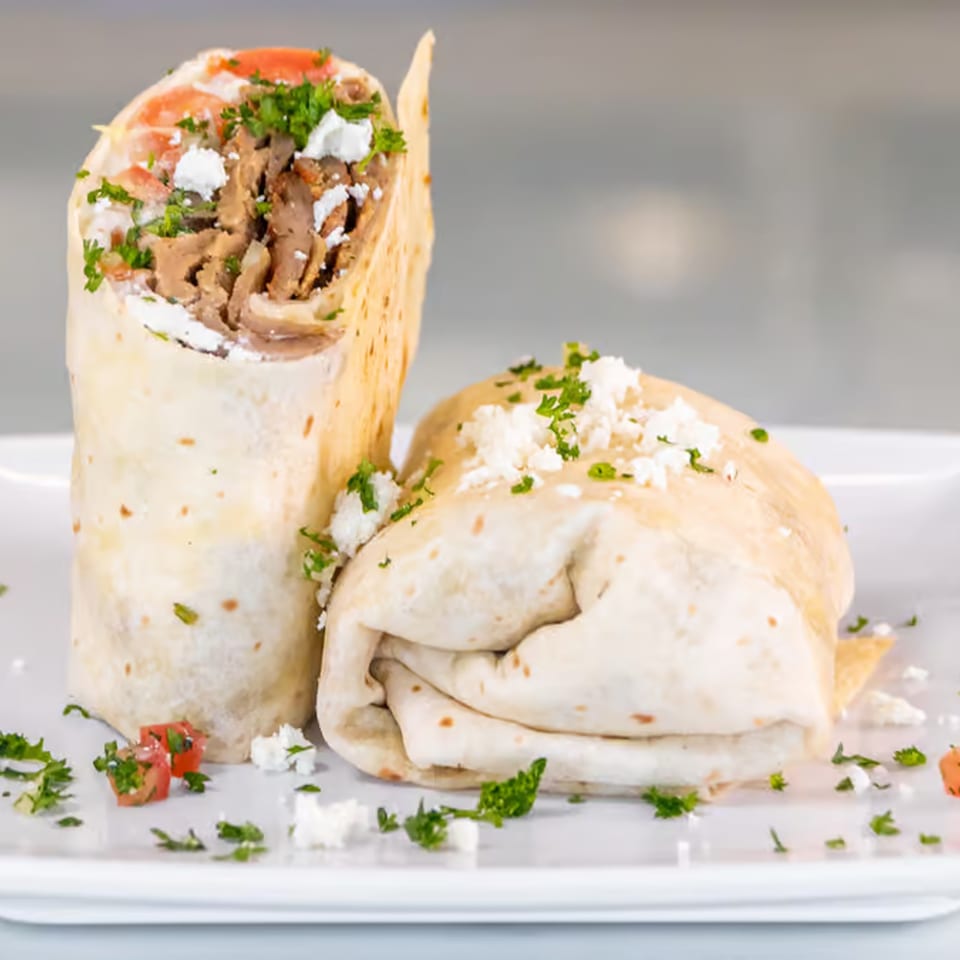 Two Greek gyros, one upright and one lying down, filled with meat, feta, tomatoes, and parsley.