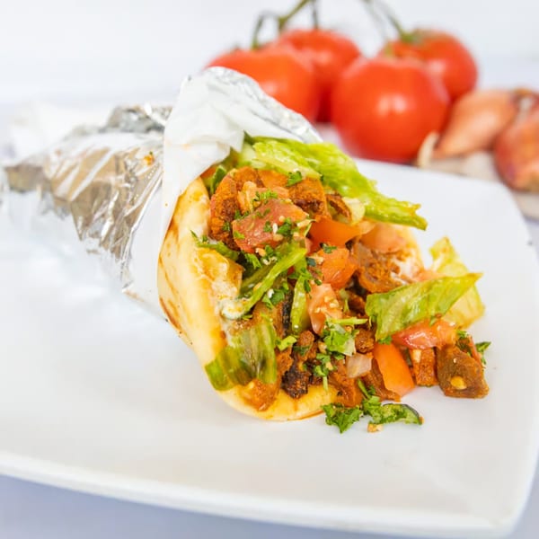 A Greek gyro with meat, lettuce, tomatoes, and sauce, partially wrapped in foil on a white plate.