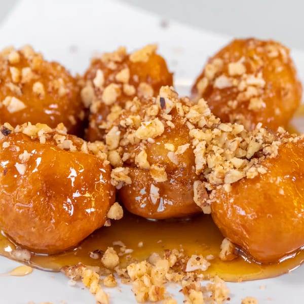 Close-up of golden Greek loukoumades, drizzled with honey and sprinkled with chopped nuts.