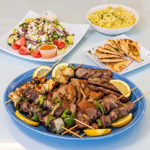 A large blue platter of Greek grilled meats, skewers, lemon, with salad, rice, and pita bread.