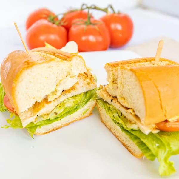 A grilled chicken sandwich, cut in half, with lettuce and tomato, on a white plate.