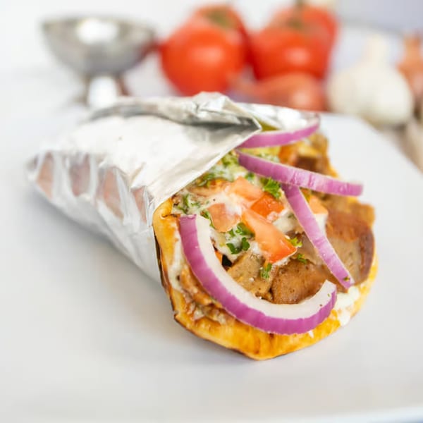 A Greek gyro with meat, red onion, tomatoes, and sauce, partially wrapped in foil.