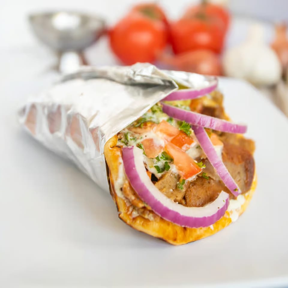 A Greek gyro with meat, red onion, tomatoes, and sauce, partially wrapped in foil.