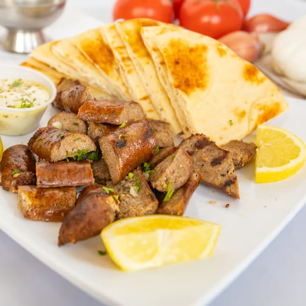 The Fat Greek's grilled Greek sausage with pita bread, tzatziki sauce, and lemon wedges.