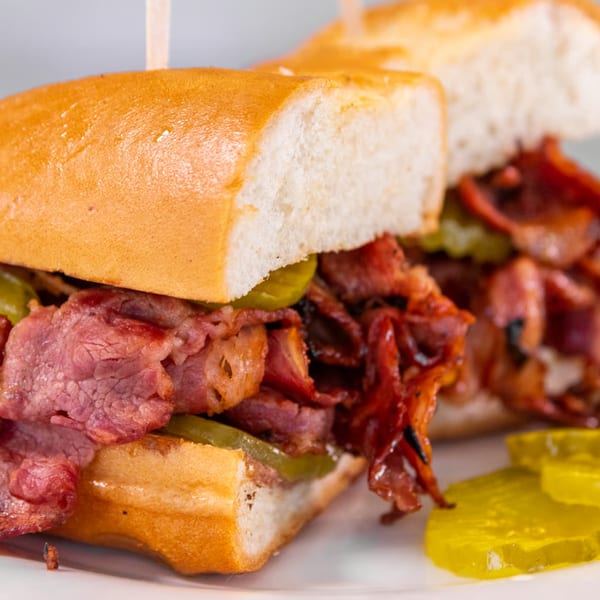 Close-up of a Greek sandwich with sliced meat, pickles, and a golden-brown bun.